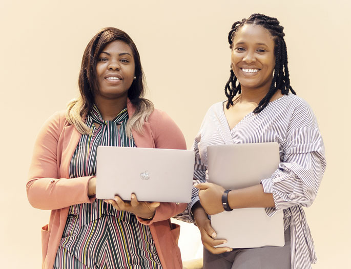 Two women carrying laptops and smiling